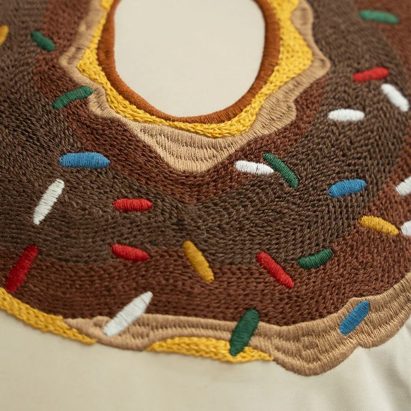 Square decorative pillow cover with hand-embroidered donut appliqué and piping Stornfield
